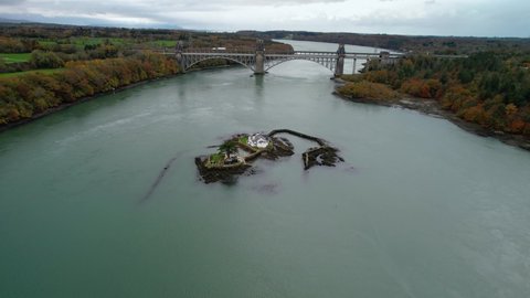 Red Weir Island or Ynys Gored Goch in Swellies Strait with Britannia Bridge in background, Anglesey in Wales, UK. Aerial forward 