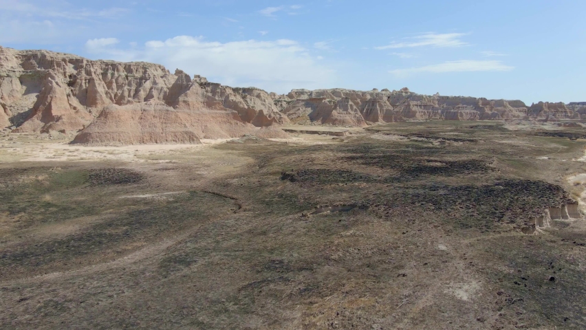 Fly over grassland in Badlands National Park, South Dakota with dirt mountains in the background