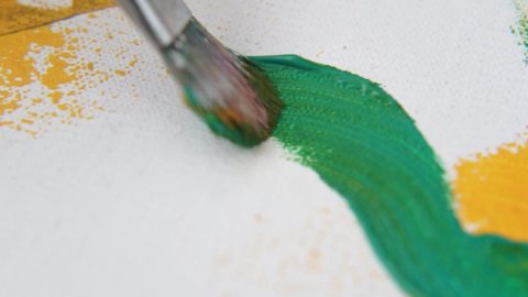 Macro shot of big paintbrush painting with green and yellow paint on white canvas.