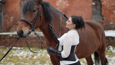 sexy lady is posing with brown stallion in horse yard of old manor in winter day, human and animal