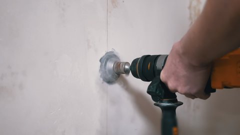 Builder Using a Puncher Makes a Hole in a Concrete Wall to Set a Power Socket. Hands. Rotation of a drill with a diamond crown on an electric rotary hammer. Dust. Installation of electrical wiring.