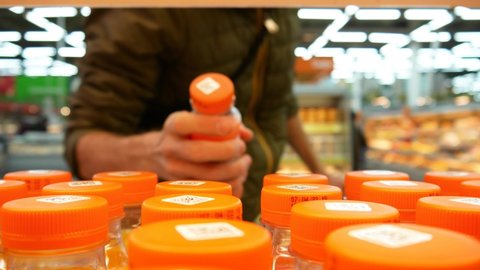 Close-up of many bottles of juice with orange caps on a store shelf and a man takes one and puts it in the shopping trolley