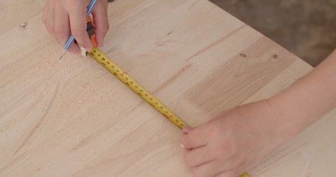 Woodworker measuring the length of wood with a tape measure and mark the point with a pencil.