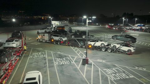 Tesla factory, Fremont, USA. Feb. 2022. Aerial footage of brand new energy efficient cars at the parking lot. Close-up shot of loaded carriage delivering electric vehicles. High quality 4k footage