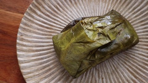 Hand unwrapping an Oaxacan Tamale made with mole wrapped in a banana leaf.