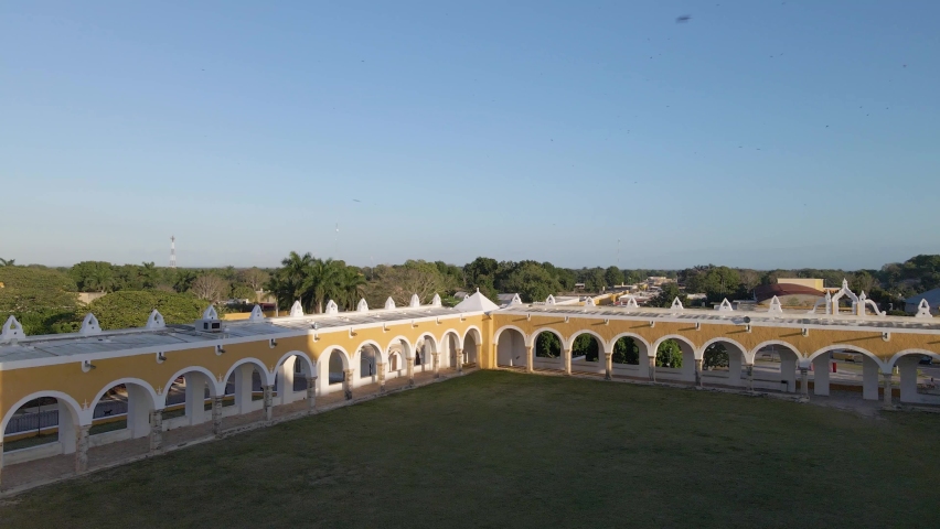 Wide angle drone shot of the beautiful yellow archways of the famous "Convento de San Antonio" with small birds flying around located in Izamal, Mexico in the state of Yucatan shot in 4k.