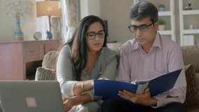 Indian Asian Middle-aged matured couple wearing Eyeglasses sitting together managing finance and keeping accounts of household expenses by calculating bills, invoices monthly expenditures using laptop - Powered by Shutterstock - Get 15% off with code: PIKWIZARD15