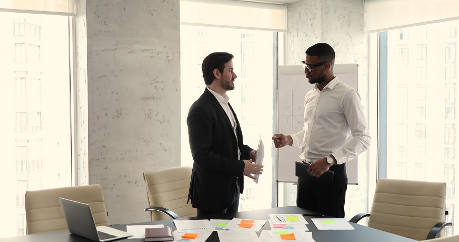 Two diverse businessmen stand at modern office meeting room talk finish negotiations confirm good deal shaking hands. African American and European males coworkers partners reach agreement handshaking Royalty-Free Stock Footage #1089340155