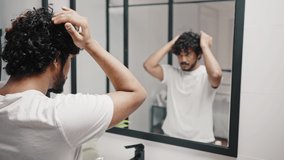 Young Asian Indian man puts foam on curly hair to fix hairstyle looking at mirror reflection in bathroom. Guy keeps daily routine in morning closeup - Powered by Shutterstock - Get 15% off with code: PIKWIZARD15