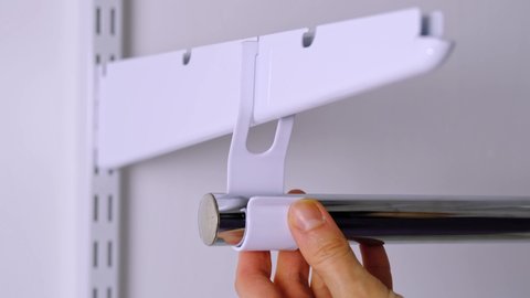 Installation brackets of a metal mesh shelf in the dressing room system on a bracket. Hands is assembling a white holder storage system close-up