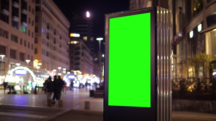 Billboard with a green screen on a background of city traffic in night time. Mockup and copy space