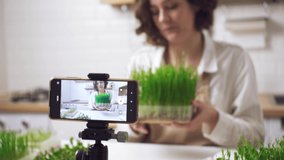 Healthy food blogger girl talking while recording video green sprouts, vlog concept, women, technology communication. Food blogger talks about benefits of microgreens in kitchen. Healthy eating, vegan