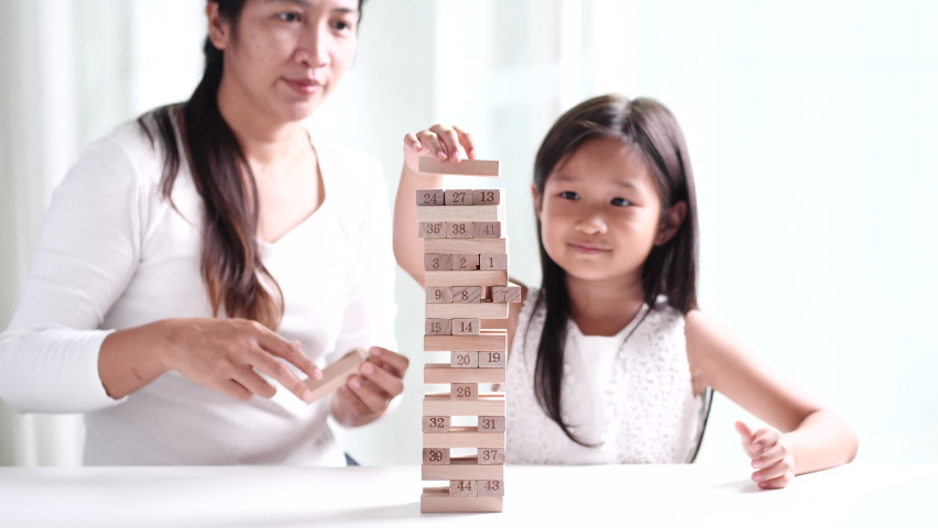 Happy family young Asian mother, child girl daughter and father spending time together, having fun, playing game Jenga wooden tower blocks at home. Concept of happy family, mothers, fathers, children