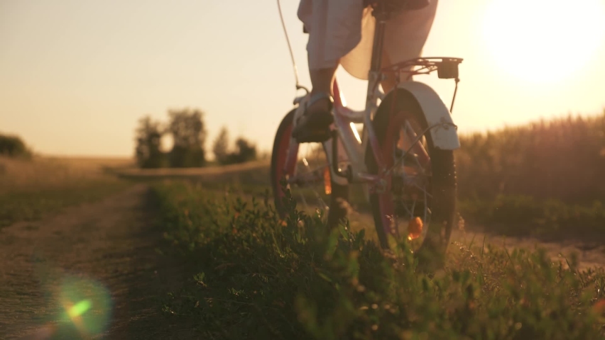 Happy family in the park. Little girl rides a bicycle. The child's feet are pedaling. The kid is riding at sunset, spinning a bicycle wheel. A chidhood dream. Physical activity, cardio. | Shutterstock HD Video #1089346591
