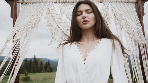 A beautiful young girl in a white long dress walks through a field at top of the mountain