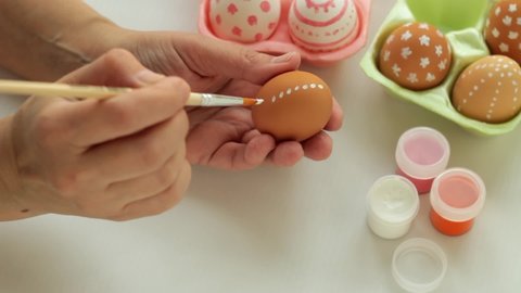 Hand of a man is painting colored Easter eggs. A girl draws a pattern on an Easter egg  with Easter eggs in the background.
