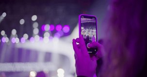 Fan Girl is Filming by Smartphone live Music Concert or Festival Event with Purple Light. Young Woman takes Video or Picture of Show Event. Blogging or Nightlife concept. 4K handheld close up shot