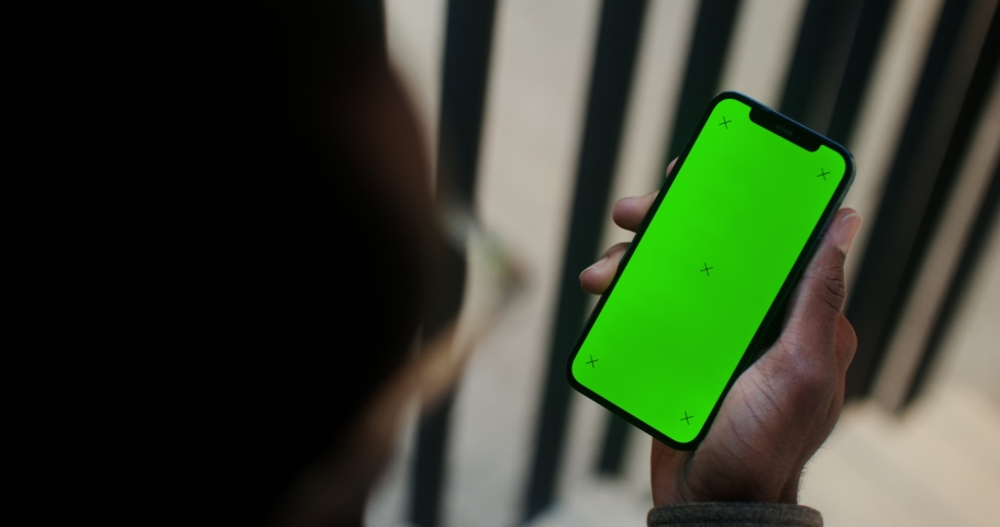 A mobile phone with a green screen in the hand of a man of African American appearance, video filming from behind, his face is not visible. Copy space, mockup, chroma key. Video in 4k, red komodo Royalty-Free Stock Footage #1089354491