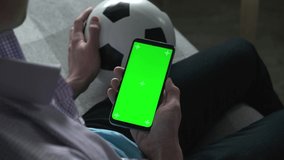 Football fan use smartphone at home with green chroma key Screen. Application At Home, Back View. Mobile App or advertisement.