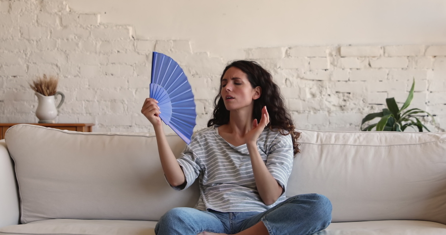 Overheated annoyed Latin woman fall on sofa too tired to cool herself with hand fan. Unhappy sweaty young lady suffer of health problem feel hard to breath at hot living room without air conditioner Royalty-Free Stock Footage #1089354871