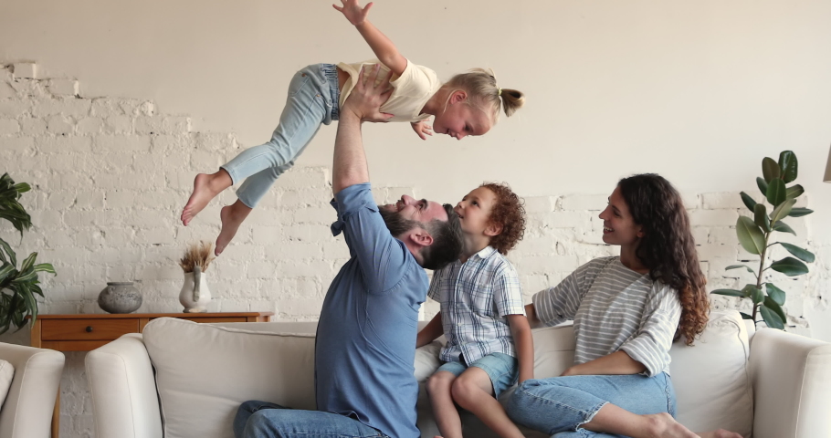 Happy mixed race family play together. Smiling young Latin mom elder son watch strong dad lift younger daughter up in air. Laughing little girl pretend flying bird in funny game with parents brother Royalty-Free Stock Footage #1089354901