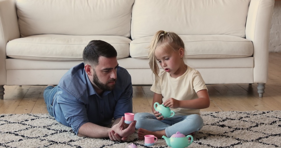 Cute little girl sit on carpet on warm floor play role game tea party with loving dad using toy teaset. Funny small daughter make imaginary coffee for dear father hold bowl act putting sugar into cup Royalty-Free Stock Footage #1089354903