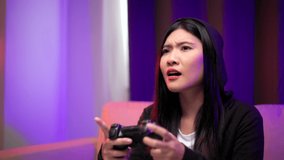Gamer losing moment. Young asian pretty woman sitting on sofa holding joystick in living room. Unhappy female Professional Streamer chinese playing game online in dark room neon light