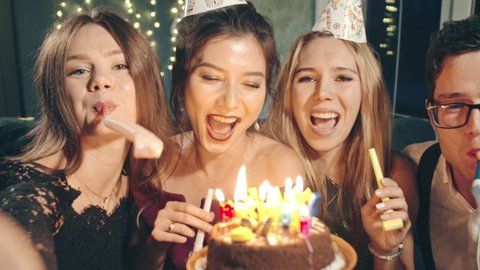 Happy multiracial friends selfie congratulating with birthday excited asian girl, giving cake, celebrating. Funny guys in holiday or birthday caps resting together, laughing, blowing whistle at party.