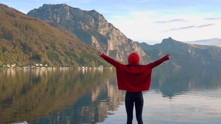 Woman hiker enjoying landscape mountain lake. smiling young slender girl standing on mountain lake background with rising hands Swiss alpine nature landscape walk in mountain alps, looks around, enjoy