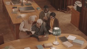 From above slowmo of senior professor of Literature and three of his students studying together at reading room of library discussing books and sharing opinion - Powered by Shutterstock - Get 15% off with code: PIKWIZARD15