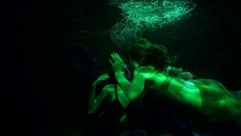 sexually lesbian mermaids are floating underwater, two women in dark depth of ocean