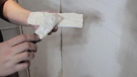 Applying glue to a white decorative gypsum brick. Brick laying on the wall, close-up