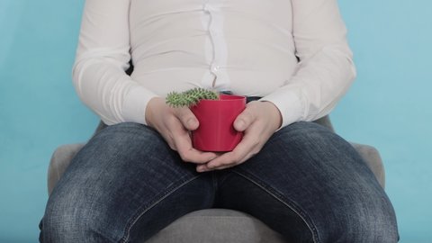 An office worker in a white shirt sits on a chair and holds a red cactus pot in his hands. The concept of chronic male diseases with a sedentary lifestyle, close-up