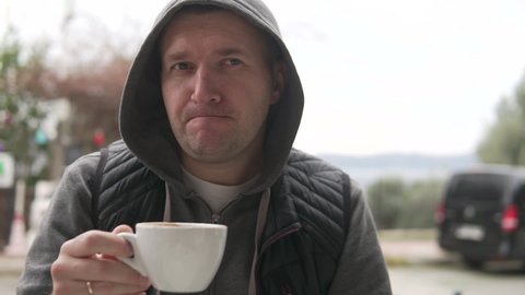 A brutal man drinks coffee at a table in a cafe on the street, close-up.