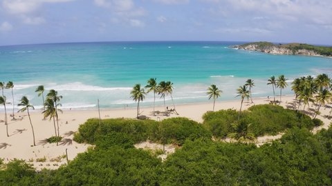 White sand palm beach and turquoise sea waves. Exotic sea beach on a summer sunny day. Green tropical peninsula coast. Travel and recreation on the paradise coast.