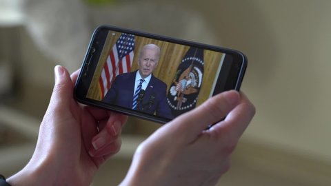 Saint Petersburg - Russia - April 16, 2022 a woman is watching the news of US President Joe Biden's speech on her phone. Close up, soft selective focus