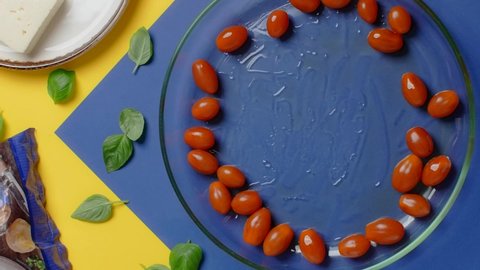 Vertical flat lay video: the cook puts feta cheese to the plae with cherry tomatoes before baking