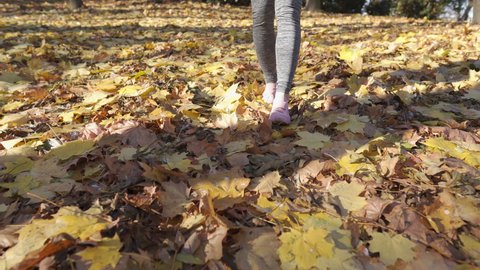 The sight of a woman's feet stepping on autumn leaves in a city park.