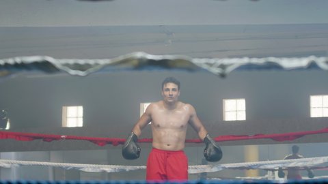 Young male boxer doing shadow fight in boxing gym while crossing ring and approaching camera, practicing punches and dodging. Athletic man enjoying sports training indoors. Sport, boxing concept