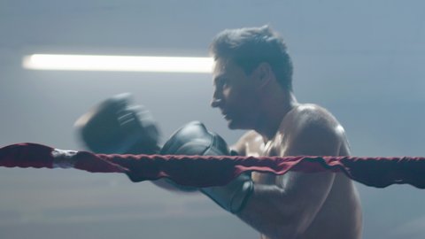 Young male boxer doing shadow fight while training in boxing ring alone. Athletic man practicing punches and dodging techniques. Sport, boxing concept