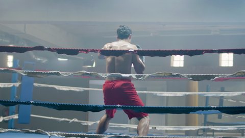 Young male boxer doing shadow fight while training in boxing ring alone. Athletic man practicing punches and dodging techniques. Sport, boxing concept