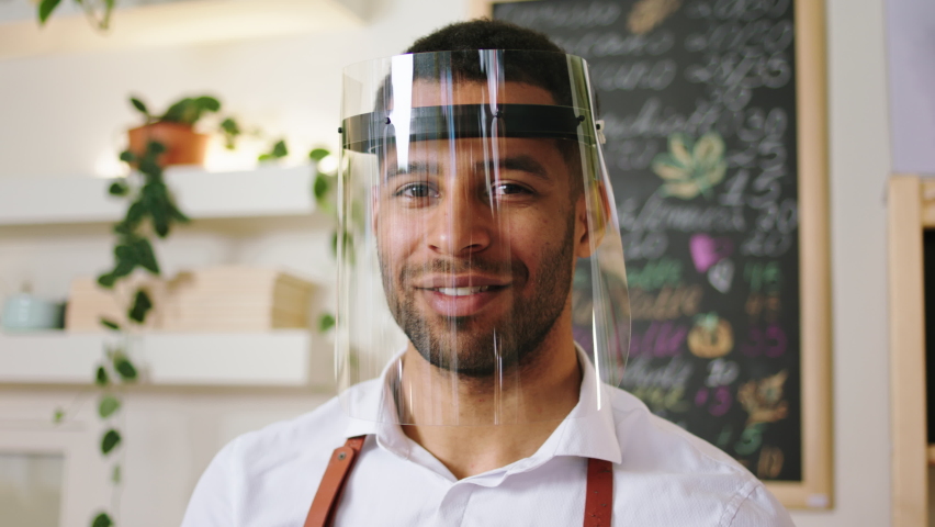 Closeup to the camera portrait of a barista man Afro American with protective mask posing to the camera smiling large Royalty-Free Stock Footage #1089367585