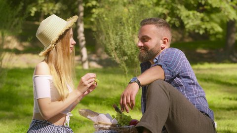 Romantic picnic concept. Happy loving woman feeding her boyfriend with grapes, enjoying lovely date in summer park, slow motion