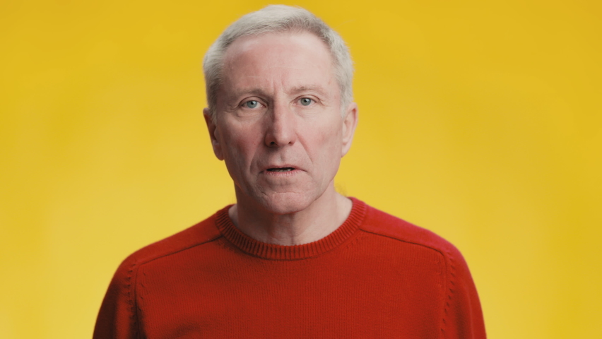 Shock and astonishment. Close up portrait of amazed grey haired senior man feeling amazed and stunned, touching his face, yellow studio background, slow motion