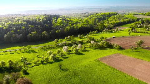 Aerial footage of scenic green landscape with meadows, hills and forests in spring, with cars driving on a road 