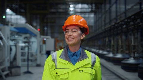 Joyful supervisor woman laughing in safety uniform say hello at modern warehouse. Beautiful joyful industrial engineer walking at manufacturing facility production. Happy brunette manager in helmet .