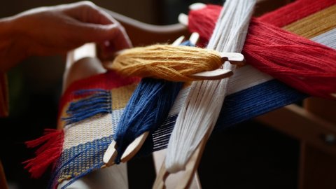 Weaver picks prepared shuttles with multicolored yarns up off the hand loom, selective focus