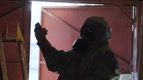 person in protective chemical suit and gas mask checking level of radiation in abandoned room in panic looks at device and quickly runs away