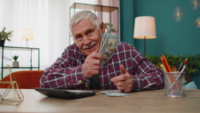 Joyful grandfather man counting calculating cash money dollars enjoying financial independence at workplace. Senior grandpa pensioner checking family financial budget, lottery win, planning expenses
