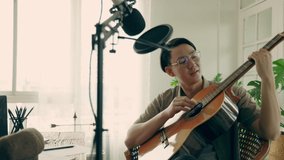 Young Asian man with short hair practice playing guitar from internet or online tutor at home. Musicians perform live music and sing through the application at home studio. self study